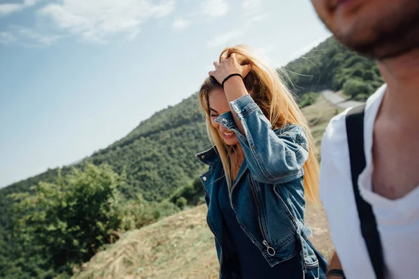 性感的热金发碧眼的牛仔裤夹克微笑 触摸她的头发 自然景观的背景 绿色森林 山脉和蓝天 — 图库照片