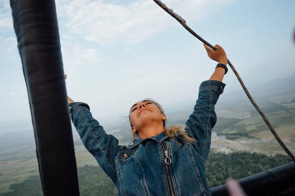 Tender young woman flying in air balloon on the big high. Leans back and rising hands. Amazing nature view from the top.