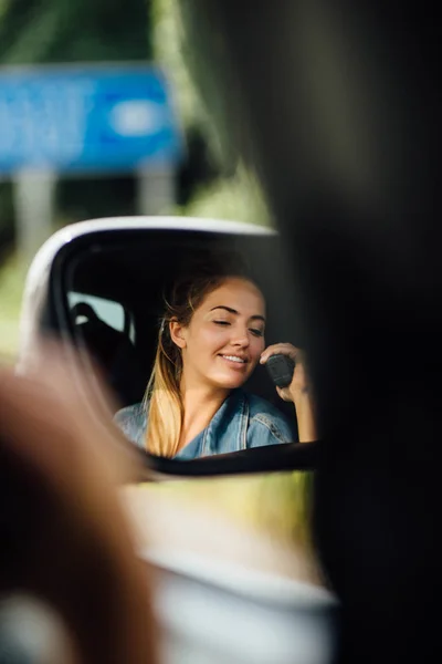 Attractive young woman in the car talking on the radio to the other people. Travelling all arounf the world. Warm autumn weather. Photo in the mirror.