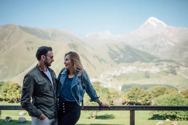 幸せな人は 愛でお互いを見る 金髪女性のジーンズのジャケット 黒のズボンを身に着けています サングラスの男 背景に印象的な山の風景 — ストック写真