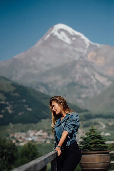 山を背景にジーンズのジャケットで魅力的な女性 雪に覆われた高峰 — ストック写真