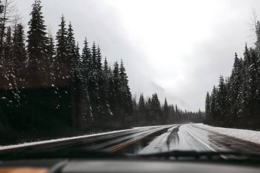 Boş yol kışın, karda taraf, gri gökyüzü çam ormanı. Sakin doğa. Kanada arabayla seyahat.