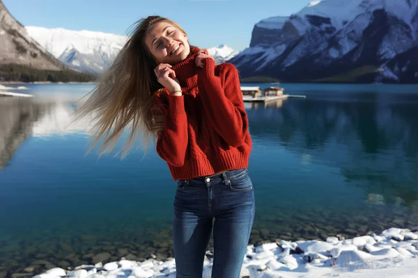 快乐的女人微笑着在湖附近的户外有乐趣 挥动着金发 自然之美 超薄牛仔裤和红色冬衣 — 图库照片