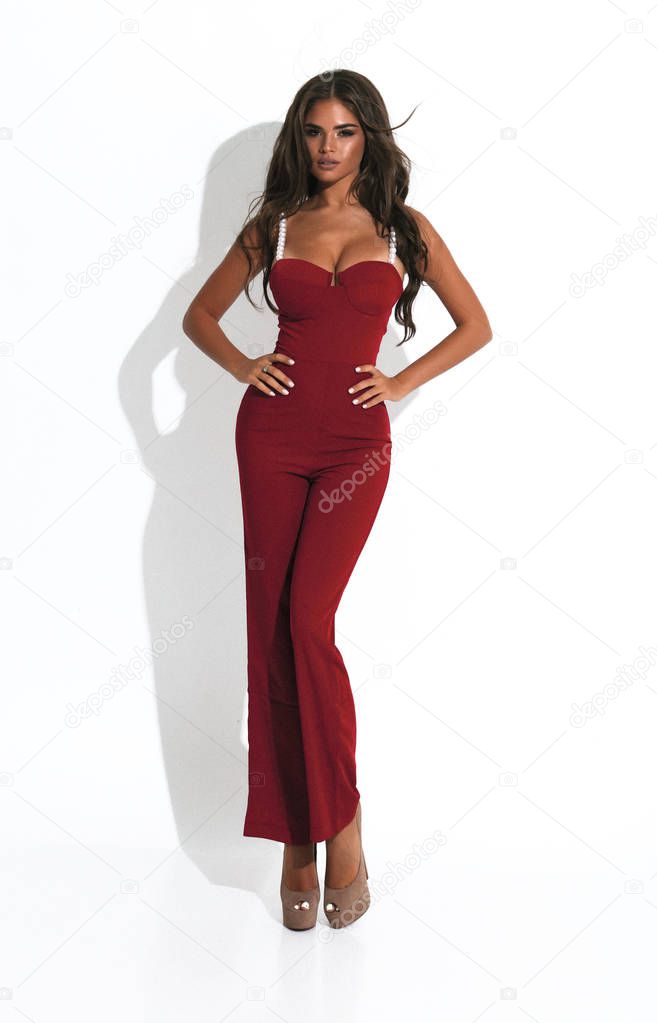 Slim lady in red suit with white straps standing in the white background. Shoes  with high heels. Brunette with long hair.