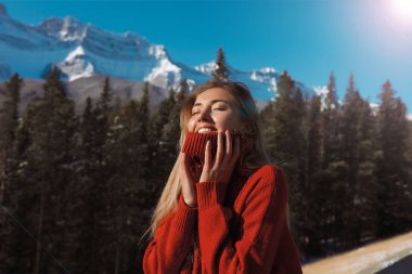 Dağ ve orman doğal güzelliği ile çevrili genç kız portresi. Yüksek tepeler beyaz kar ve saf mavi gökyüzü ile kaplı. Kırmızı sıcak kazaklı, sabit soğuk Kanada kış için hazır sarılmış 