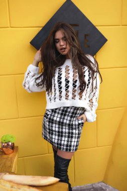 Yeni sonbahar koleksiyonu moda giysiler giyiyor, çekim için dergi ve reklam güzel genç kız. Uzun kıvırcık saç modeli ve şık makyaj. Kahve masasının üstüne yalan baget.
