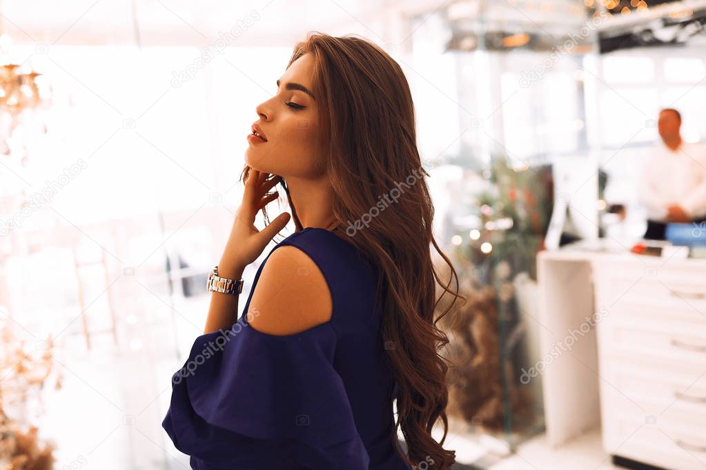 Elegant brunette girl standing in the blue cocktail dress, closed eyes, long beautiful hair. Accessories on hand open shoulders. Stylish look, shooting for the magazine. Tender skin and pretty face.