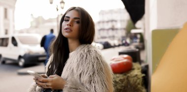 Büyük dudaklar ve moda makyaj oturma ellerini, onun telefon ile açık süslü genç kızla manifatura. Esmer uzun saç omuz üzerine uzanarak. Hay yalan büyük lezzetli turuncu kabak. Sonbahar göz