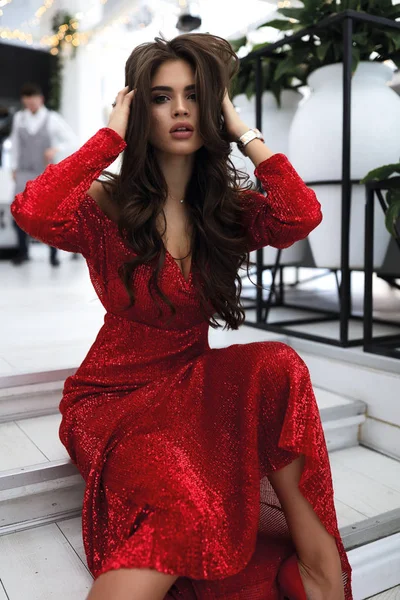 Luxury woman wearing stylish party dress with sparkles. Touching her dark curly hair, looking straight. Perfect fashion look, long hairstyle and modern bright makeup on the face. Big lips, dark eyes