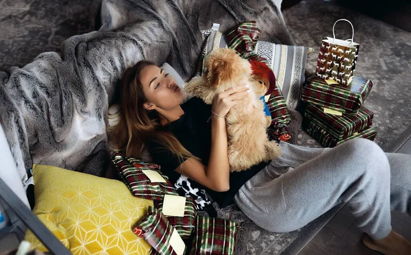 Curlies と彼女のかわいい子犬を女性のペットにキス 友人や家族からのプレゼントの中でソファに横たわっています 遊んで 一緒に楽しんで クリスマス休暇 温かみのある家庭的な雰囲気 — ストック写真