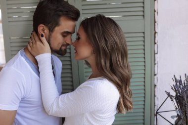 Erkek ve kadın beyaz bluz ayakta birlikte Windows yeşil Panjur yakınındaki. Kadın eli erkek yüzünde onu öpmek istiyor. Koyu esmer saçlı, sakallı adamın yüzünde. Aşk ve tutku 