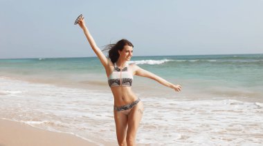 Mutlu kadın yalnız Sahilde yürüyüş. Eğleniyor ve yaz hava keyfini çıkarın. Arka plan mavi okyanusta. Yukarı, gülümseyen, makyaj yüzünde, esmer saçlar rüzgarda sallayarak ellerini koymak.