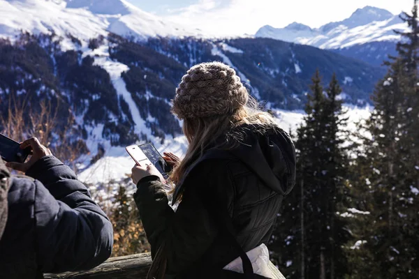 旅游女子穿着暖和的衣服 站在观景台上 在周围拍摄不可思议的自然美女照片 高山强大的山脉和茂密的松树林 很多白雪 — 图库照片