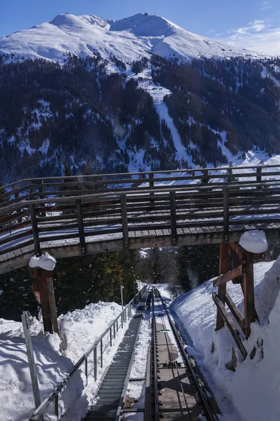 View from the top of the mountain on the wooden bridge, under the bridge is lying railway. A lot of white snow on the sides. High hills with dense forest, pure blue sky. Winter holidays in Europe.