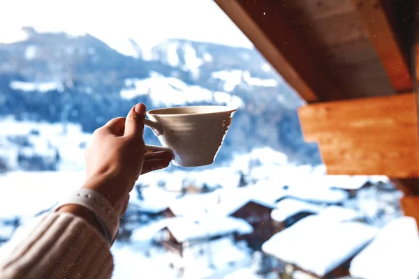 おいしいコーヒーの朝のカップを持っている女性の手が柔らかきます 雪の山 背景の建物の屋根 冬の温かい飲み物 スイス連邦共和国の居心地の良い雰囲気 — ストック写真