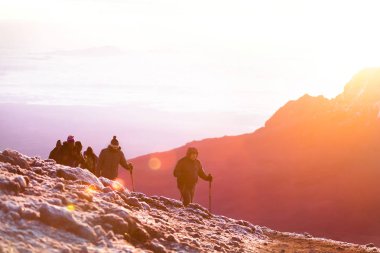 Dağlarda parlak güneş ışığı. Doğa inanılmaz manzara. Kilimanjaro'nun tepesine tırmanan bir grup insan. 5000 metre yükseklikte soğuk rüzgar ve kar. Unutulmaz macera