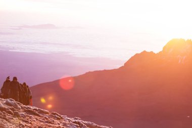 İnanılmaz doğa güzelliği, dağlarda gün doğumu. Dağın tepesine tırmanan insanlar. Sarı sıcak ışık ve 5000 metre yüksekliğinde dondurucu soğuk. Sıcak spor giyim ve ekipman, kayalarda kamp.