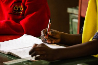 Bir kalem tutan ve okulda ders hakkında yeni bilgiler yazma çocuk elleri yakın çekim resmi. Not defterindeki kağıdı temizleyin. Öğrenciler dinler ve notalar yapıyor. Öğretmen tema açıklayan.