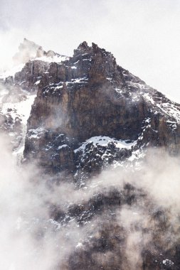 Yüksek tehlikeli zirveleri ile güçlü siyah dağ, karla kaplı. Dağın etrafındaki beyaz bulutlar. Etkileyici doğal manzara. Üstte soğuk ve aşırı tırmanış.