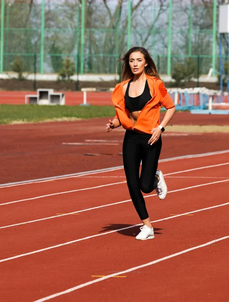 Summer morning workout outdoor on the sport stadium. Young woman running on the track, preparing for the marathon. Comfortable and modern black leggins on her slim body. Long hair waving behind.