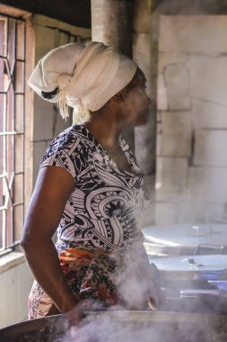 Geleneksel Afrika kıyafetleri, kafasında atkı. Ailesi için yemek pişiren bir kadın. Lezzetli aroma ve buhar mutfak etrafında yayıldı. Afrika'yı dolaşın ve başka bir yaşam tarzı görün.
