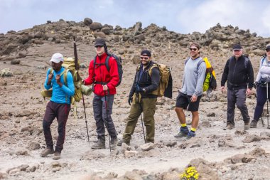 Mutlu turistler dağ ekipmanları ile tepenin yakınında duran, sıcak rahat giysiler giyiyor. Üç gün boyunca dağa tırmanma, yorgun ama Afrika doğanın manzarasının tadını çıkarın.