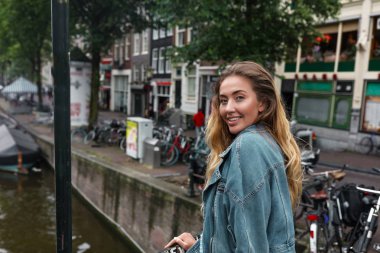 Mutlu genç model köprüden aşağı yürürken, Avrupa'ya onu küçük bir gezi sahiptir. Arkada yatan sarı saçlar, yüzünde şık makyaj. Modern kot ceket giyiyor. Cafe ve kahve mekanları arkasında. 