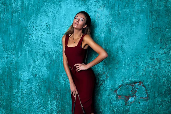 Passion girl with long blonde hair demonstrate new stylish burgundy dress. Slim perfect body, bronze skin, long arms. Fashionable look, beautiful face with bright makeup.Hand on the waist, accessories