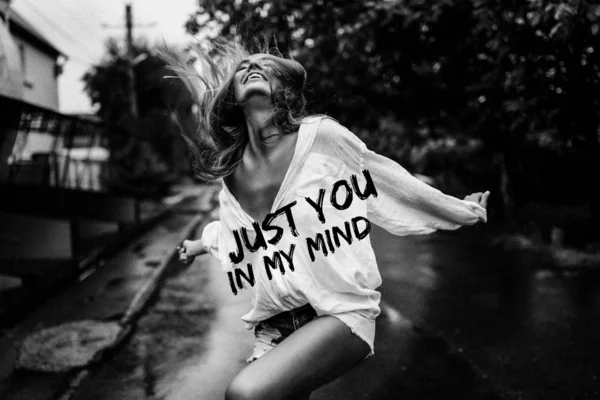 Romantic girl dancing outdoor under the summer rain. Wearing oversize white shirt and sexy jeans shorts. Title on the photo, black and white style. Smiling and having fun alone in wet clothes.