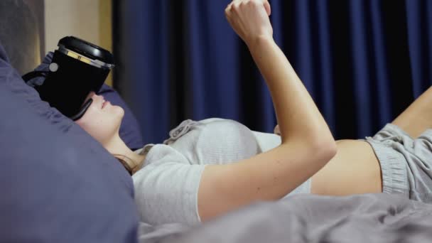 Mujer joven acostada sobre almohadas en la cama el uso de la realidad virtual, ver vídeo VR — Vídeo de stock