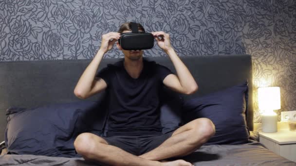 Homem vestindo VR Headset sentar na cama. Olhando em volta. Assista vídeo VR — Vídeo de Stock