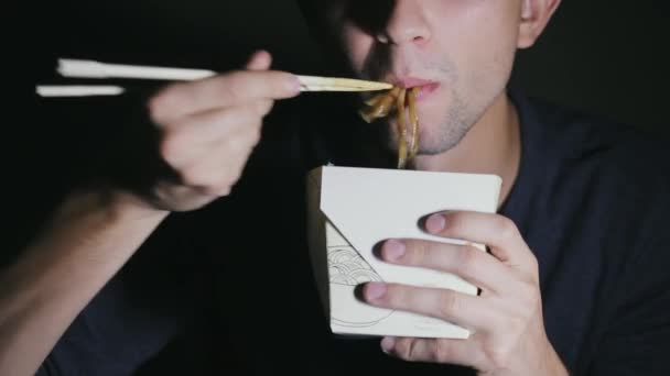 Primer plano de un hombre que está comiendo fideos con palillos de una caja. Europea comer comida china — Vídeo de stock