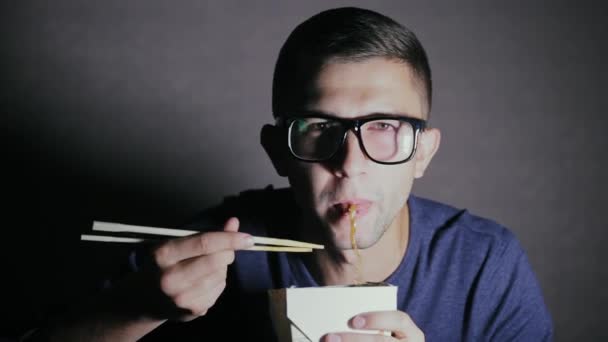 Primo piano di un uomo che sta mangiando tagliatelle con le bacchette da una scatola. Mangiare europeo cibo cinese — Video Stock