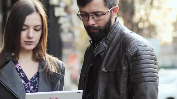 ビジネスの男性と女性に路上で、手のタブレット デバイスを立って話す何かを見て、. — ストック動画