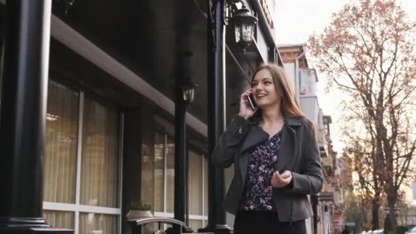 Attractive caucasian businesswoman walking on the street on the office building background, talking on the phone. Emotional speak outdoors — Stock Video