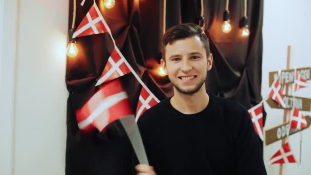 Retrato del joven viajero alegre sosteniendo la bandera danesa, agitando y sonriendo mirando a la cámara . — Vídeos de Stock