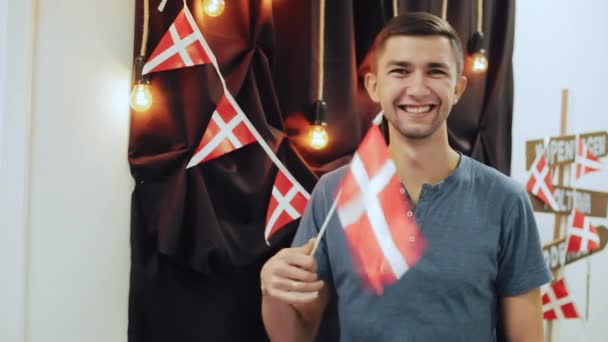Πορτρέτο του happy ταξιδιωτών νέος άνθρωπος που κρατά δανική σημαία, κουνώντας και χαμογελά βλέπουν φωτογραφική μηχανή. — Αρχείο Βίντεο
