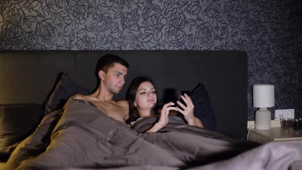 年轻夫妇上网, 并使用躺在床上的智能手机上的应用程序 — 图库视频影像