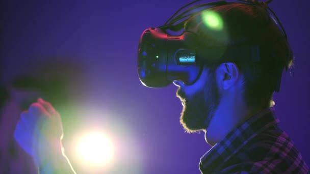 El hombre barbudo utiliza la pantalla de auriculares VR para el videojuego de realidad virtual en el club vr. Gira la cabeza y mirando a su alrededor, destello de luz en el fondo — Vídeo de stock