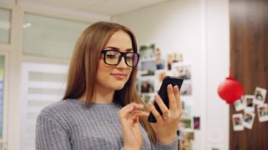 Yakın çekim portre gözlüklü genç kadın ofiste smartphone kullanın. Metin mesajı, dalga köpüğü online