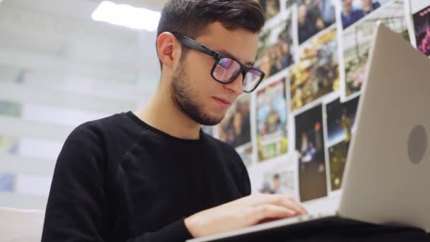 Zár-megjelöl szemcsésedik-ból fiatal stílusos üzletember szemüveget, gépelés a smartphone és a laptop, irodai háttér — Stock videók