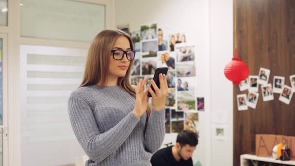 Mujer joven en gafas de uso smartphone en la oficina. Mensaje de texto, navegación en línea, aplicación, red social . — Vídeos de Stock