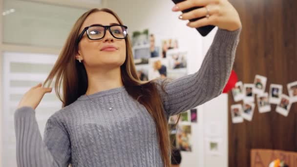 Encantadora mujer con gafas sonriendo en la cámara mientras hace selfie en la bonita sala de oficina . — Vídeos de Stock