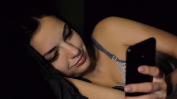 Mooie vrouw gebruik mobie app terwijl liggend in bed in de slaapkamer 's nachts, kijkt foto — Stockvideo