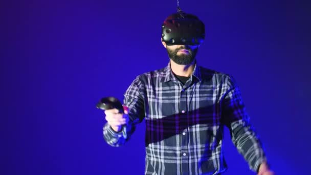 Hombre barbudo usando auriculares modernos de realidad virtual con mando a distancia, controles remotos, clics, trabajo del hombre en VR, gesticulando con las manos, fondo azul — Vídeo de stock