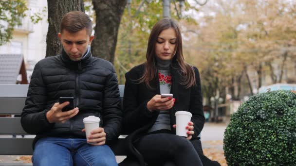 Amici che navigano in internet, bevono caffè e parlano seduti su una panchina, per strada — Video Stock