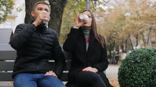 Pareja joven tomando café y hablando sentada en un banco, en la calle — Vídeos de Stock