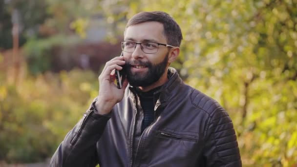 髭の男は、日当たりの良い秋の公園で携帯電話を使用してください。. — ストック動画