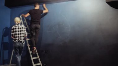 Graffiti sanatçıları bir kontur mavi bir duvara çizer. Bir adam merdivenlerde bir duvar çizimi için hazırlar..