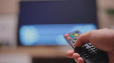 Erkek el televizyon kumandasını tutuyor ve televizyon kanallarını değiştiriyor..